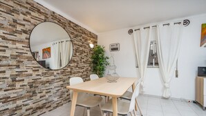 A room with a wooden table, white chairs, a round mirror, a brick-patterned wall, a potted plant, and a sign indicating WiFi availability.