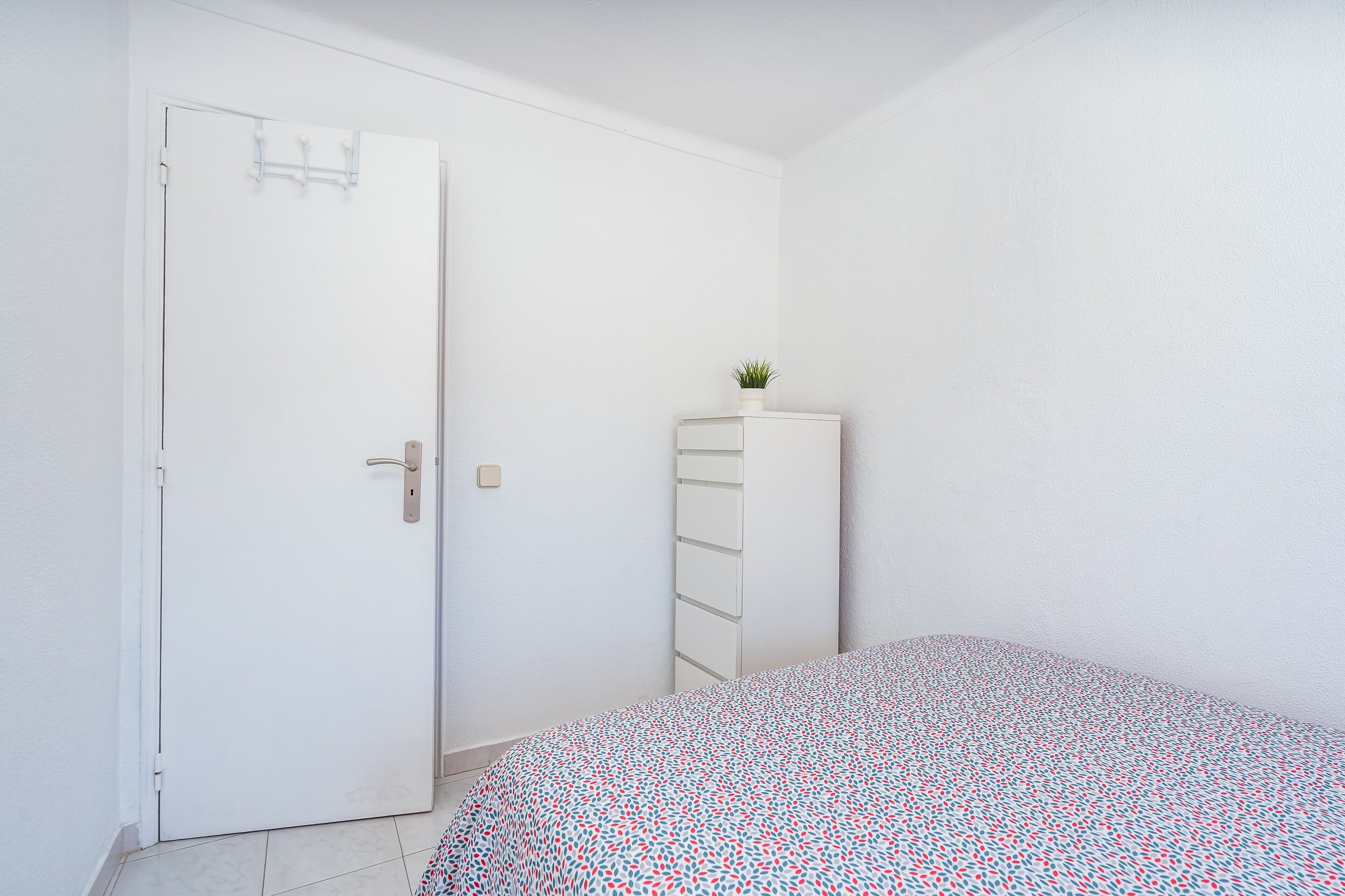 Un dormitorio con una cama, un armario blanco, una planta pequeña y una puerta.