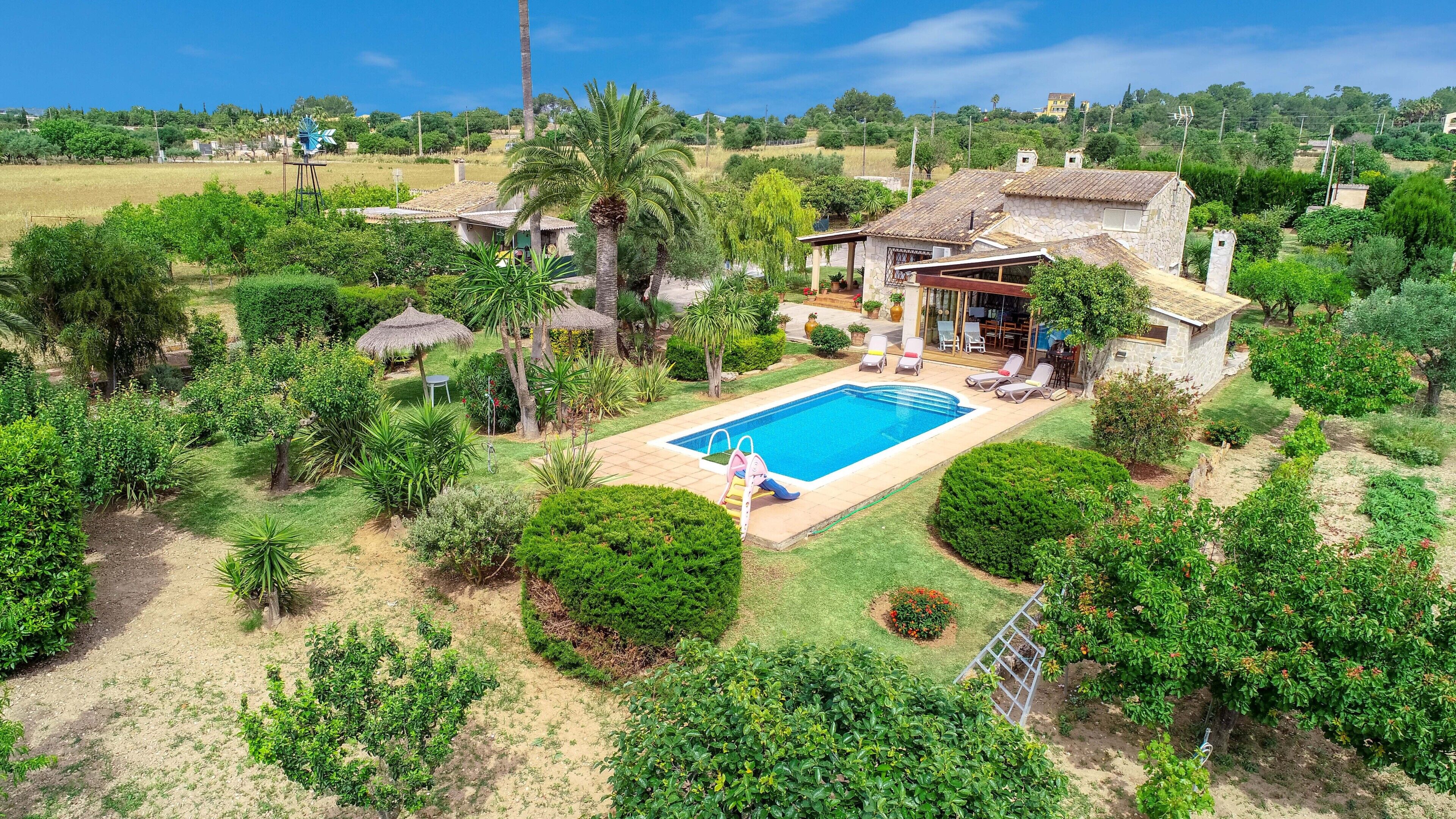 Una propiedad residencial con piscina, un patio con sillones de descanso y una casa de piedra.