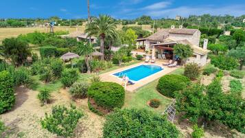 Una propiedad residencial con piscina, un patio con sillones de descanso y una casa de piedra.