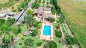 Una propiedad residencial con piscina, un patio con sillas de descanso y un jardín con diversas plantas y árboles.