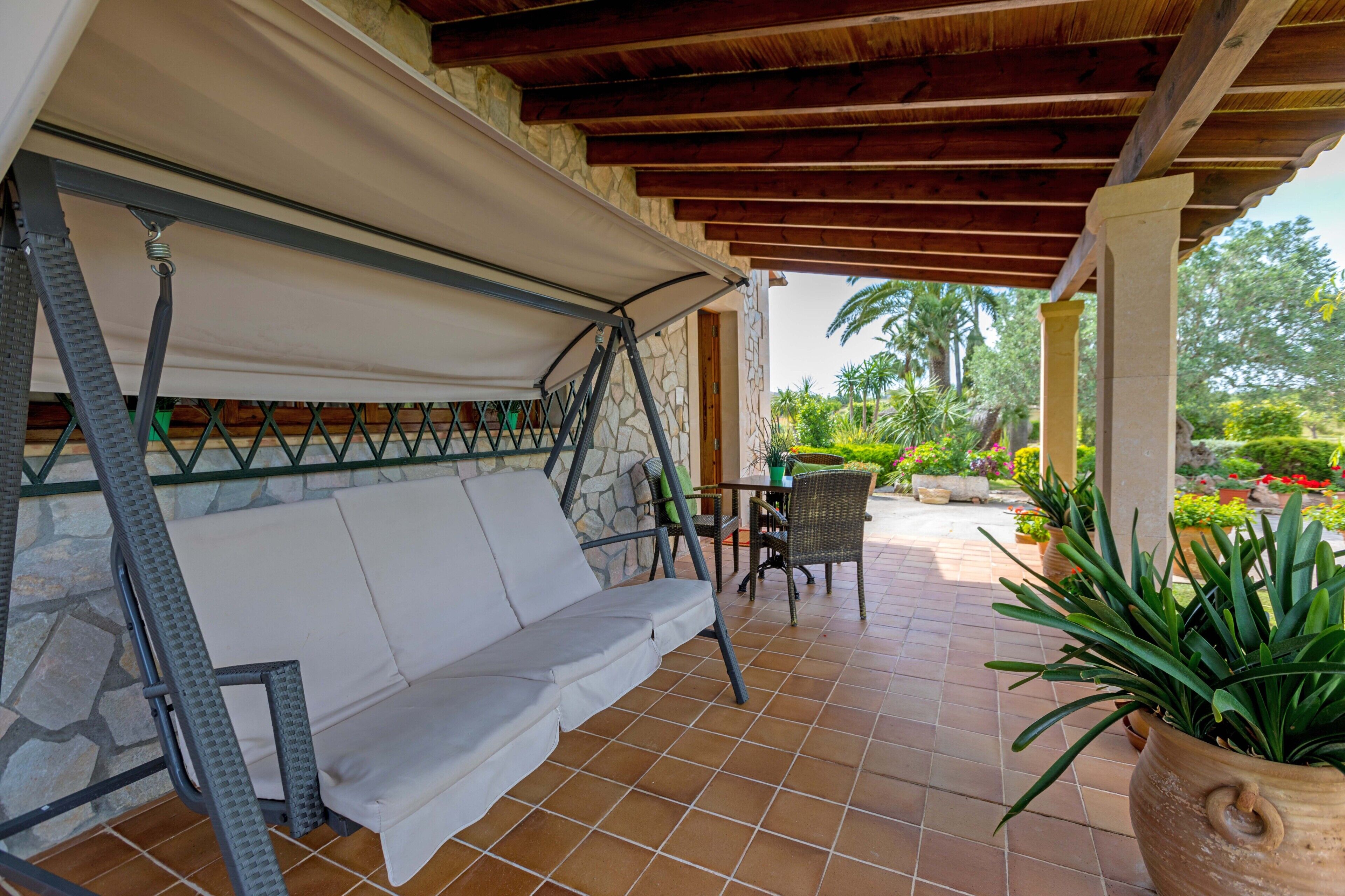 Ein überdachter Patio-Bereich mit Schaukelstuhl, Tisch und Kübelpflanzen.
