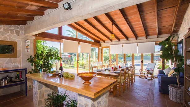 Una cocina amplia con una isla central, paredes de piedra, vigas de madera y ventanas grandes.