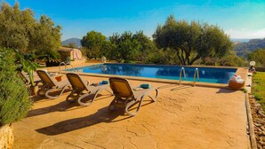 Una piscina rectangular con agua cristalina y azul, rodeada por una terraza empedrada con sillas de descanso.