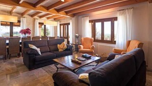Un salón amplio con un sofá oscuro, una mesa de centro de madera y un ventanal con cortinas.