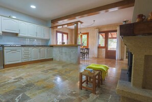 Uma cozinha espaçosa com armários brancos, piso de pedra e um espaço de jantar com mesa e cadeiras.