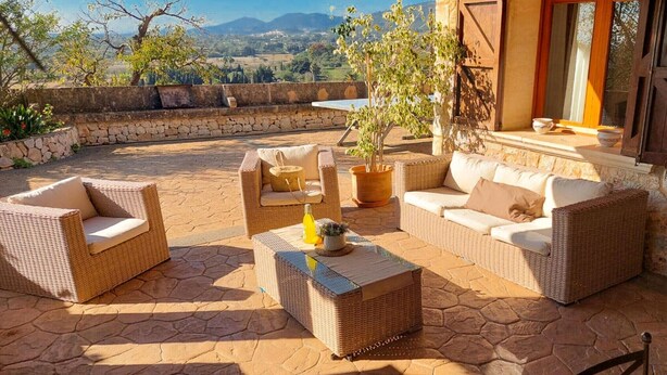 Un patio al aire libre con mobiliario de mimbre, una planta en maceta y un muro de piedra.