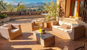 An outdoor patio with wicker furniture, a potted plant, and a stone wall. - Country House 'Maribel' with Mountain Views, Private Pool and Wi-Fi (Inca)
