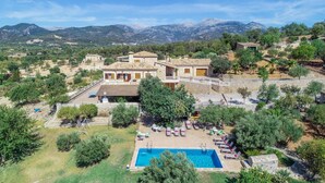 Una villa con piscina, mobiliario exterior y montañas al fondo.