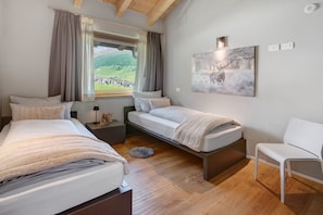 A bedroom with two beds, a chair, a window with a view, and a painting on the wall. - Chalet 'Spark Chalet e Spa Livigno' with Mountain View and Private Spa (Livigno)