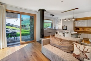 Una cocina moderna con una isla central, un comedor con mesa y sillas, y un amplio ventanal corredero que da a un patio exterior.