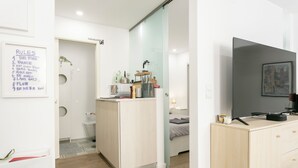 A modern, minimalist bedroom with a wooden dresser, a TV, and a bedside table.