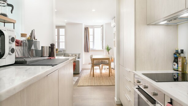 A modern kitchen with a central island, built-in oven, and a dining area with a table and chairs.