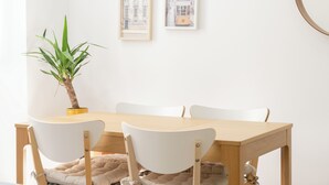 A dining area with a wooden table, white chairs, a potted plant, and framed pictures on the wall.