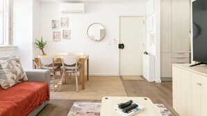A modern living room with a sofa, a dining table with chairs, a TV, and a kitchen area.