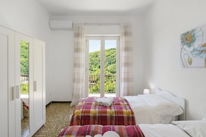 A bedroom with two beds, a large window with curtains, a painting on the wall, and an air conditioning unit. - Apartment 'Vista Mare A Due Passi Dal Sentiero Degli Dei' with Sea View, Wi-Fi and Air Conditioning (Agerola)