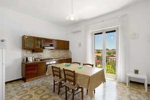 Una cocina con armarios de madera, una mesa de comedor con sillas, una ventana con cortinas y vistas a edificios.
