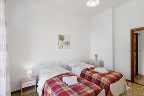 Een kamer met twee bedden, een nachtkastje, een lamp, een schilderij en een deur.