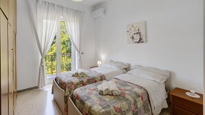 A bedroom with two beds, a window with curtains, a bedside lamp, and a wall-mounted air conditioner. - Apartment 'Familiare A Due Passi Dal Sentiero Degli Dei' with Sea View, Wi-Fi and Air Conditioning (Agerola)