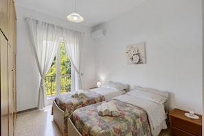 A bedroom with two beds, a window with curtains, a bedside lamp, and a wall-mounted air conditioner.