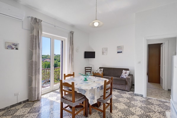 Ein Essbereich mit Tisch und Stühlen, einer Couch, einem Fernseher und einem Balkon mit Blick.