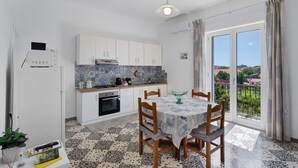 A kitchen with white cabinets, a tiled backsplash, a dining table with chairs, and a view through a glass door. - Apartment 'Familiare A Due Passi Dal Sentiero Degli Dei' with Sea View, Wi-Fi and Air Conditioning (Agerola)