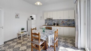 A compact kitchen with white cabinets, a tiled backsplash, and a dining area with a table and chairs. - Apartment 'Familiare A Due Passi Dal Sentiero Degli Dei' with Sea View, Wi-Fi and Air Conditioning (Agerola)
