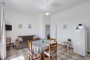 Ein kompakter Wohnbereich mit Esstisch, einer Couch, einem kleinen Fernseher und einem Kühlschrank.