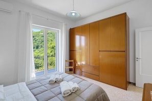 Ein Schlafzimmer mit Bett, Schrank, Stuhl und einem Balkon mit Blick.