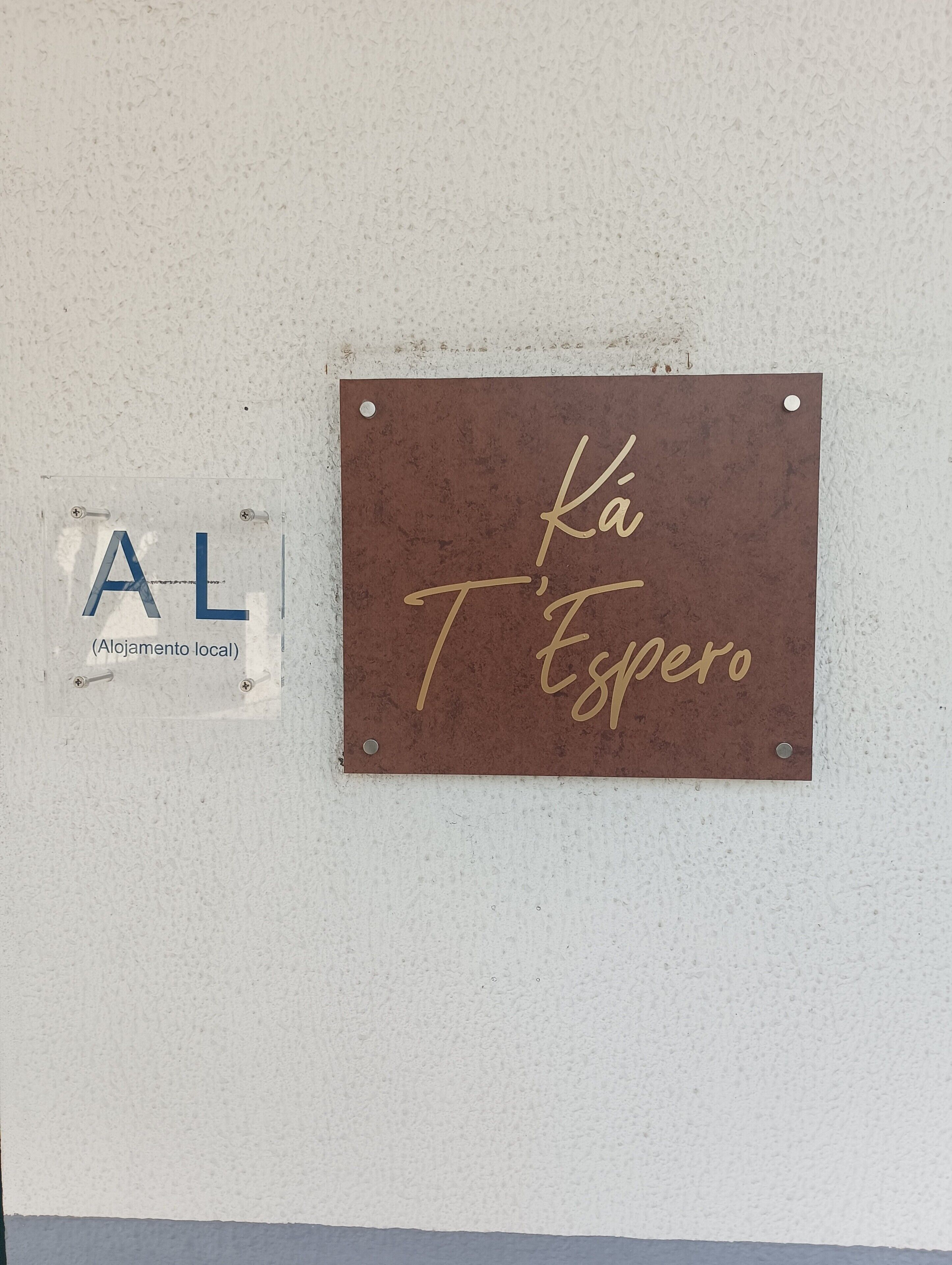 A wall-mounted sign with 'Ka T'Espero' written in gold script, and a smaller sign with 'AL' and 'Alojamento local' in blue.