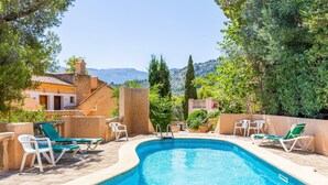 Une piscine entourée de bâtiments et d’arbres, avec des chaises longues à proximité.