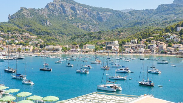 Un port de plaisance abritant de nombreux bateaux, avec une chaîne de montagnes en arrière-plan et une ville côtière.