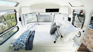 Un dormitorio compacto y bien iluminado con cama, almohadas y una ventana que da a vistas de vegetación.