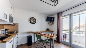A compact kitchen with a dining area, a TV mounted on the wall, and a view of the outside through a sliding door.