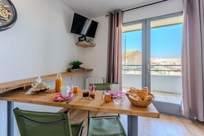 Une table de petit-déjeuner avec des chaises, un téléviseur et une vue sur un bâtiment par la fenêtre.