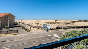 A coastal road with a building on the left, a pedestrian crossing, and a sandy beach in the background.