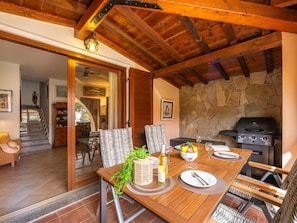 Una mesa de comedor de madera dispuesta con platos, cubiertos y una botella de vino, con una pared de piedra y una parrilla al fondo.