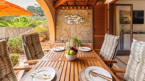 A wooden dining table set for four with a stone wall backdrop, outdoor seating, and a stone fish decoration. - Cozy Holiday Home "Casa Oleandro" in Villasimius – Relaxation & Comfort Near the Sea (Villasimius)