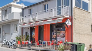 Un bar con terraza, una motocicleta estacionada al frente y un edificio con balcón.