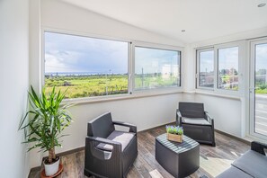A balcony with wicker furniture, a potted plant, and a view of a green landscape.