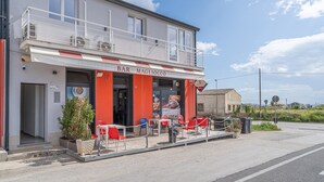 Un edificio de dos pisos con balcón, mesas al aire libre y un letrero que dice 'BAR MAGLIOSCO'.