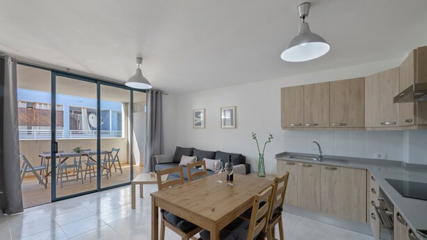 A modern kitchen with wooden cabinets, a dining table with chairs, and a sliding glass door leading to an outdoor area.