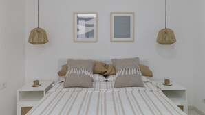 A bedroom with a bed, two bedside tables, two hanging lamps, and two framed pictures on the wall.