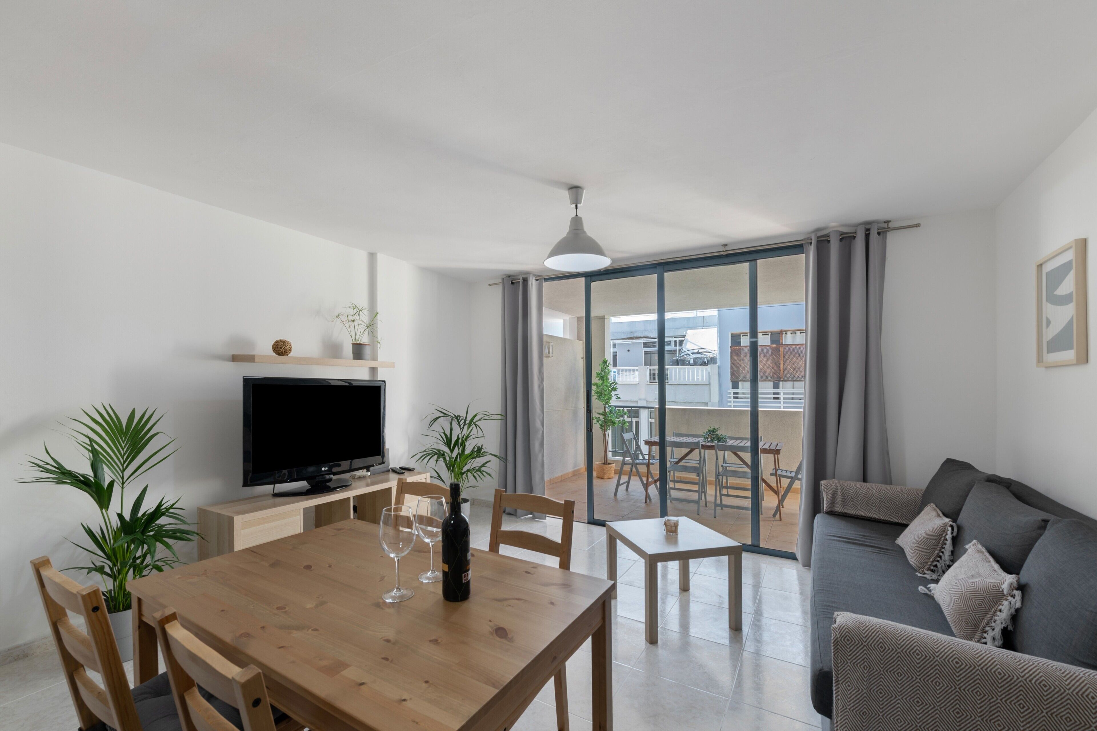 A modern living room with a flat-screen TV, wooden dining table, and a sofa.