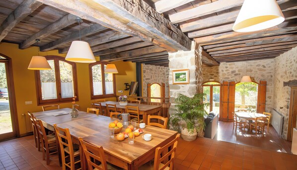 A dining area with wooden tables and chairs, stone walls, and a large potted plant.