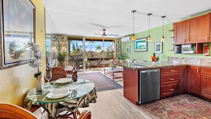 A spacious kitchen with a glass dining table, wooden cabinets, and a view of the outdoors.