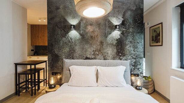 Una habitación de hotel moderna con una cama grande, una mesa de comedor y una zona de cocina al fondo.