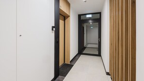 Un pasillo moderno con un revestimiento de madera, una puerta negra y piso de baldosas.