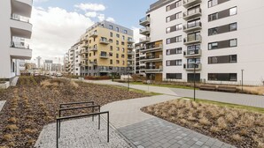 Un moderno complejo de apartamentos con varios balcones, un sendero pavimentado y una zona ajardinada con grava y césped.