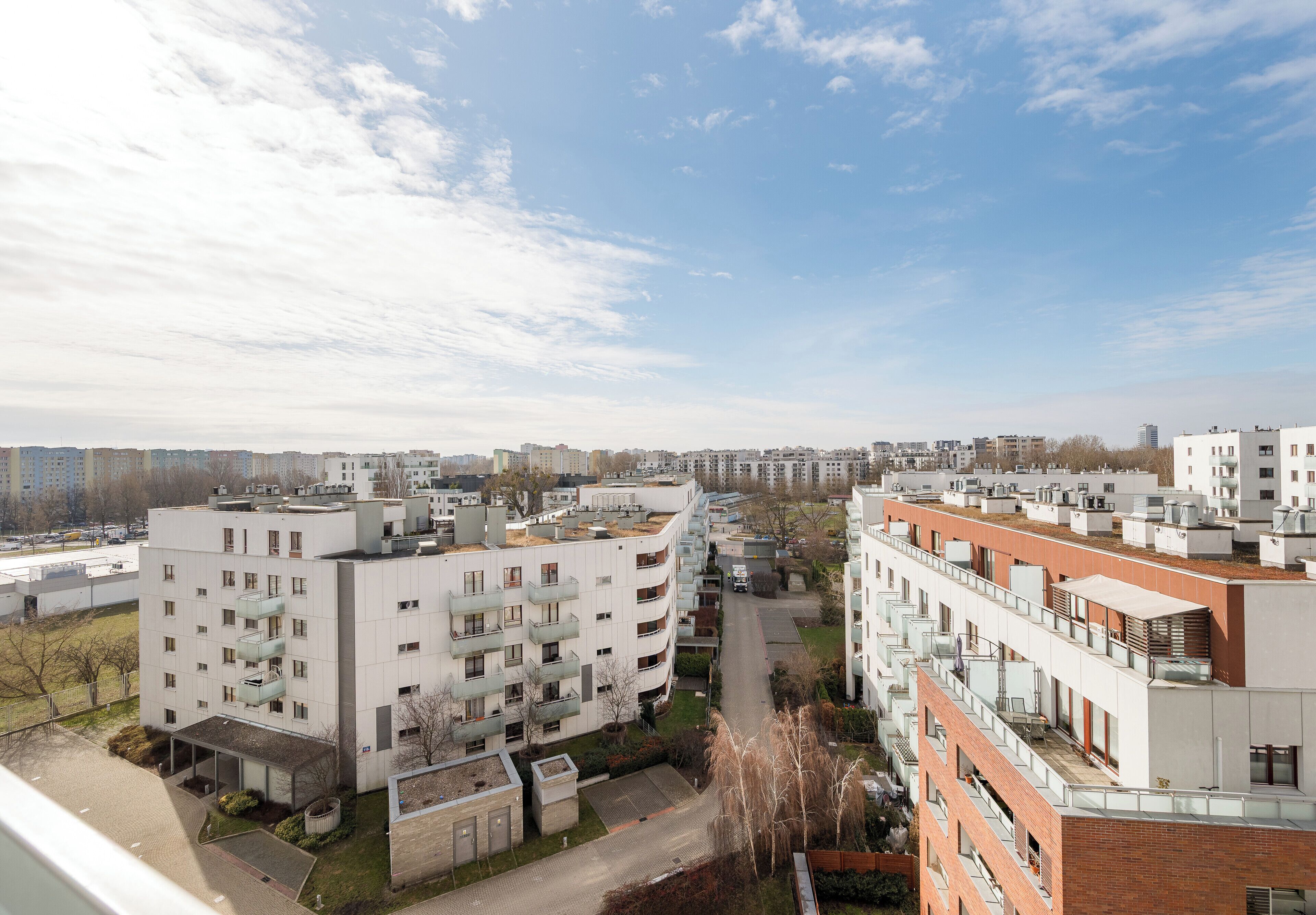 Een modern wooncomplex met meerdere appartementen gebouwen, een centraal voetpad en een heldere lucht.